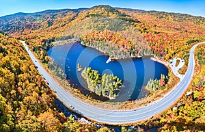 Wide panorama aerial over highway through stunning peak fall foliage New Hampshire mountains around blue lake