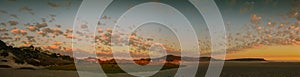 Panorama of pink and gold clouds over the beach at sunset