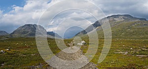 Wide panorama of Kungsleden hiking trail path with red marked stones in beautiful wild Lapland nature landscape with green bushes