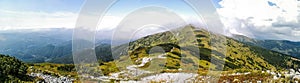 Wide panorama photo of high mountains with clouds and greenery