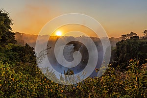 Wide panorama of victoria falls at sunset with orange sun in the sky