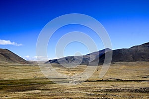 Wide panoramic view of a dry barren desert land with roads mountains and blue sky