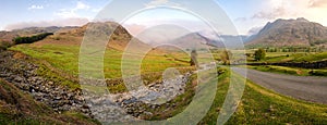 Wide panoramic view of langdale valley in Lake District with mountains in the distance and a road