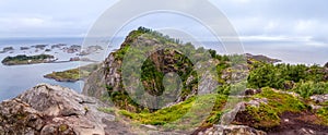 Wide panoramic view from top of cliff range over the ocean and on blue panorama of mountains and Reine in Lofoten islands, Norway