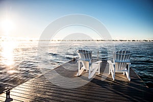 Wide photo of Muskoka Chairs on a dock with sun rising and mist photo
