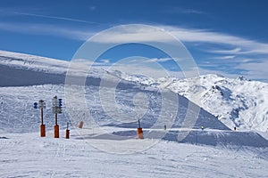A wide piste, with signposts, highlighting the name of the piste and the direction of the piste, on a clear sunny day in Meribel