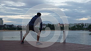 Wide rear view shot of unrecognizable sporty man preparing and warming up body before doing training, stretching legs