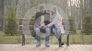 Wide shot, adult Caucasian woman taking smartphone of husband or boyfriend, looking at screen and leaving. Angry