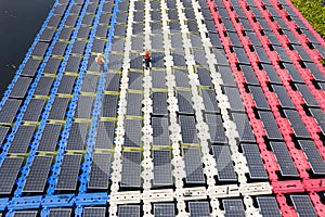 Wide shot of aeroview or top view of two technician workers walk along the solar panel system over water resirvoir for green