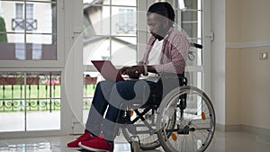 Wide shot African American disabled male freelancer typing on laptop keyboard in slow motion messaging online. Confident