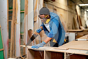 Wide shot of African American man as carpenter use saw to cut timber in factory or workplace with happiness and express smiling