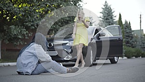 Wide shot of angry young Caucasian woman walking to victim hit by car, talking and gesturing. Stressed female driver and