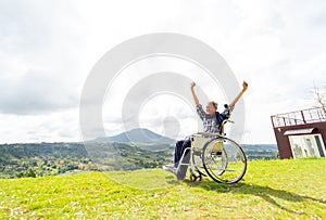 Wide shot of Asian senior man sit on wheelchair and action of raise his hands up like stretching also stay near cliff with