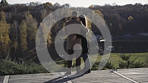 Wide shot back view of happy hugging Caucasian couple standing on wooden bridge in countryside talking. Relaxed man and