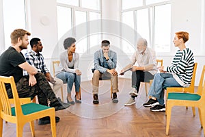 Wide shot of bearded aged professional male mentor leader counselor coach speaking at diverse business meeting with team