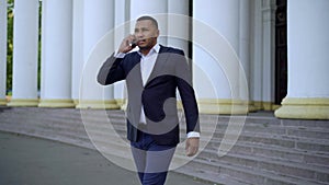 Wide shot of busy businessman talking on the phone walking out the building with columns outdoors. Concentrated