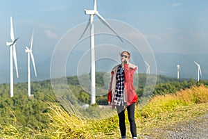Wide shot of Caucasian woman with red coat and sunglasses stand near the roadside and use mobile phone on mountain near windmill