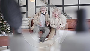 Wide shot of cheerful senior couple sitting on couch talking and laughing. Portrait of happy relaxed Caucasian husband