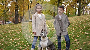 Wide shot confident boy and girl looking at camera standing with purebred dog on park meadow. Happy positive relaxed