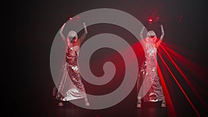 Wide shot confident female performers in costumes with red neon light dancing at black background moving simultaneously