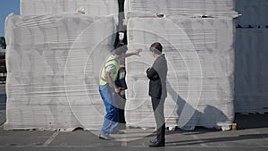 Wide shot confident Middle Eastern warehouse worker in uniform persuading Caucasian inspector in suit talking pointing