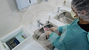Wide shot of Doctor wash dental instruments with a brush under a stream of water