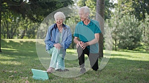 Wide shot fit senior couple working out outdoors watching online lesson talking smiling. Positive confident Caucasian