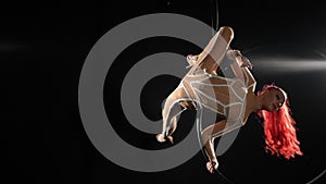 Wide shot flexible slim woman hanging on air hoop doing tricks as partner entering helping. Caucasian skilled performer