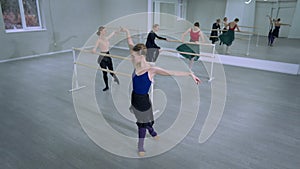 Wide shot flexible slim young ballerina putting leg down looking at camera smiling. High angle view of confident