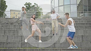 Wide shot of four Caucasian people dancing on urban stairs in urban city. Portrait of confident young men and women