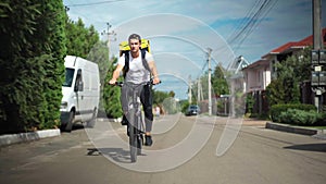 Wide shot front view confident delivery boy driving bicycle fast on sunny street in town. Caucasian handsome man