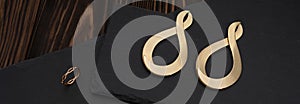 Wide shot of golden infinity symbol shape earrings and ring on dark stone surface