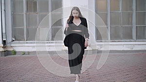 Wide shot of gorgeous slim Caucasian young woman walking to camera and leaving. Portrait of confident stylish