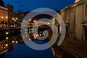 Wide shot of grass and buildings by a canal in the city of Otary-Shi in Japan during nighttime