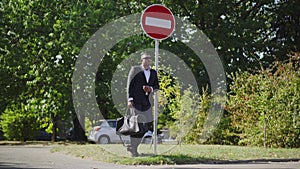 Wide shot of handsome African American man in suit and sunglasses standing in sunlight leaning against no entry traffic