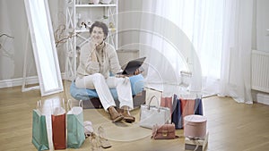 Wide shot of happy brunette middle-aged Caucasian woman sitting on bag chair with tablet looking at camera smiling