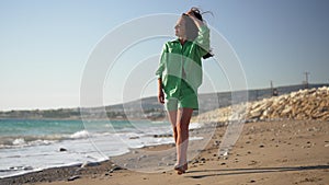 Wide shot of happy Caucasian tanned woman in green walking along sea coast in slow motion smiling. Gorgeous slim