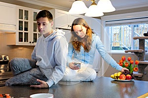 Wide shot of a happy couple in pajamas sitting at kitchen table with man drinking mug of coffee and woman with feet up