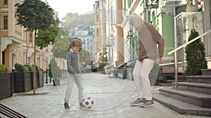 Wide shot of happy grandfather and grandson playing football outdoors on city street and giving high-five, Portrait of