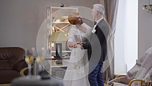 Wide shot happy senior couple of newlyweds dancing in slow motion indoors smiling. Loving Caucasian groom and bride