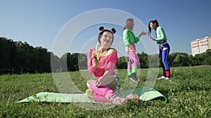 Wide shot happy woman peeling banana sitting on exercise mat with blurred women laughing pointing making fun of friend