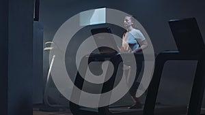 Wide shot of healthy beautiful Caucasian woman running on treadmill. Portrait of strong brunette sportswoman jogging in