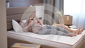 Wide shot husband and wife lying on bed turning back to back in slow motion. Portrait of Caucasian couple resting in new