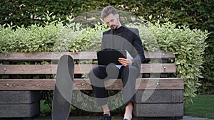 Wide shot intelligent young businessman planning business strategy sitting on bench with skateboard. Portrait of smiling