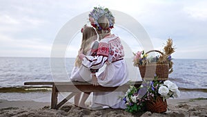 Wide shot loving Ukrainian mother hugging charming daughter admiring beauty of nature sitting on river bank. Back view