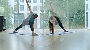 Wide shot of man and woman practicing yoga in gym. Portrait of male and female yogi doing exercises on exercise mat