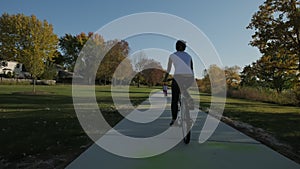 Wide shot of Mother and daughter ride bicycles in a park and on a suburban street on a sunny day. Slow motion