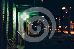 Wide shot of a neon green cross light signage hanging from a wall at night in a city