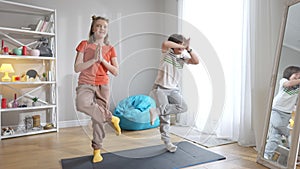 Wide shot portrait of cheerful Caucasian boy and girl standing in tree pose on exercise mat. Joyful brother and sister