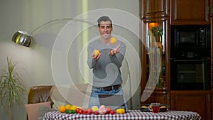 Wide shot portrait of cheerful Middle Eastern man juggling oranges at home in kitchen. Happy smiling young handsome chef